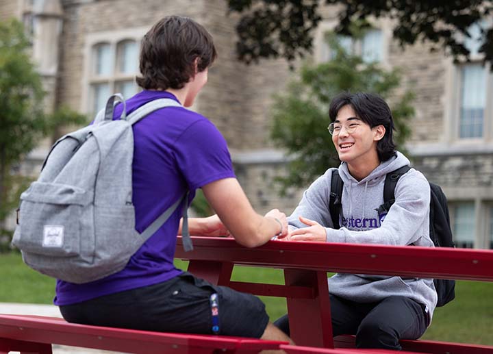 Male student talking to another student outside on a bench